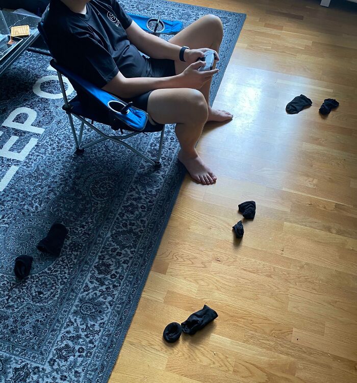 Boyfriend sitting in a chair playing video games, scattered socks on the floor.