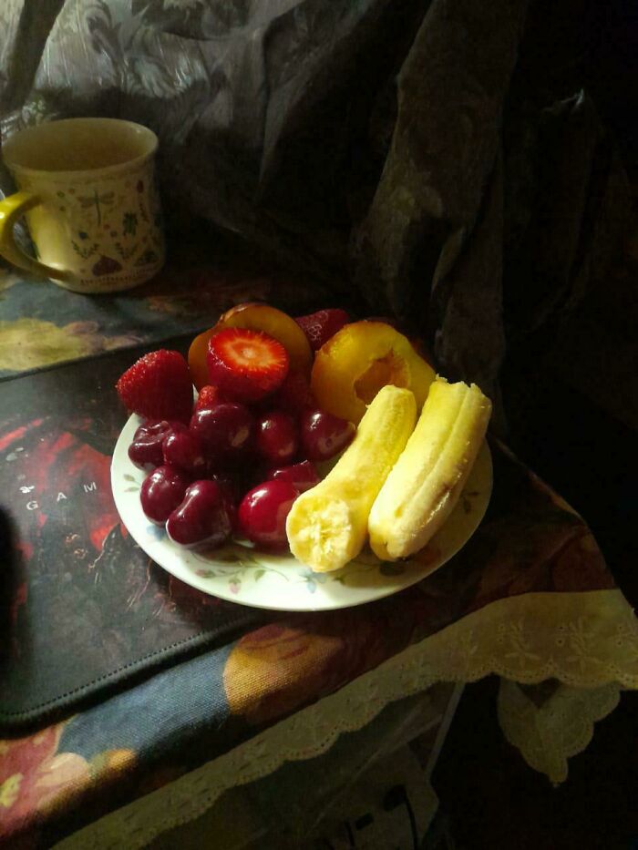 Plate of fruit resembling Renaissance painting, with cherries, strawberries, banana, and a mug in a dimly lit setting.