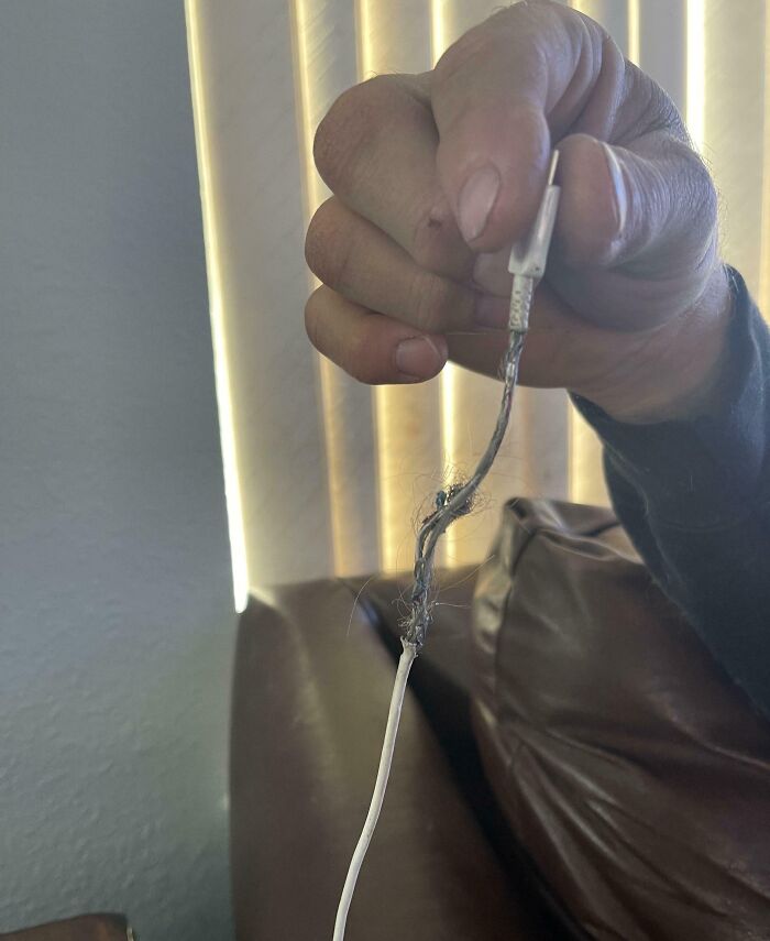 A person holding a damaged charging cable with exposed wires, showcasing a common infuriating issue with boyfriends or husbands.