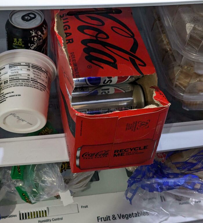 A partially filled soda box inside a refrigerator, with empty cans placed back carelessly.