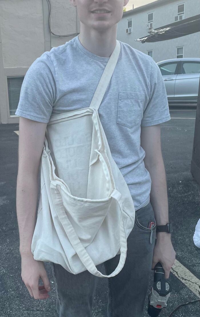 Boyfriend wearing a tote bag awkwardly as a shirt, standing outdoors holding a power drill.