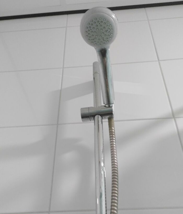 Shower head installed incorrectly by boyfriend or husband, facing the ceiling on white tiled wall.