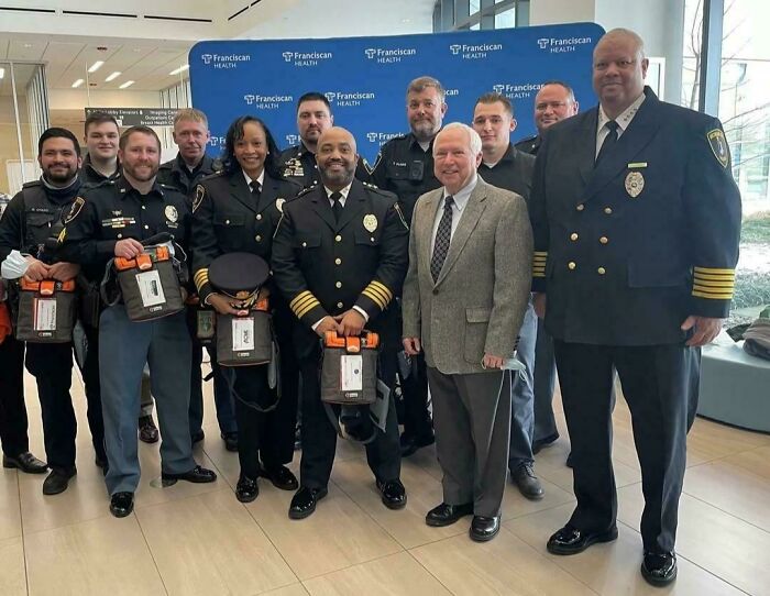 Group of uniformed officers posing with a civilian, showcasing absolute units in front of a Franciscan Health banner.