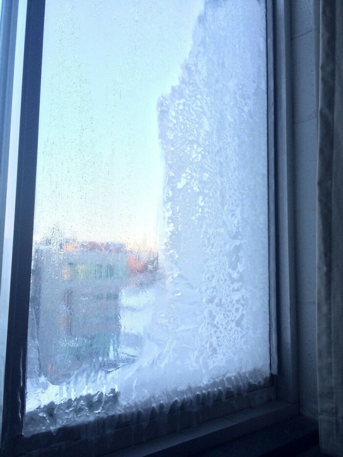 Frost-covered window showing a blurry view of buildings, illustrating ice-cold winter conditions.