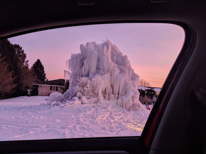 Massive ice formation in a winter landscape, viewed through a car window, under a pink sunset sky.