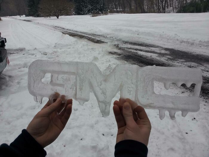 Hands holding an ice sculpture of a car logo on a snowy winter road, showcasing ice-cold winter scenery.