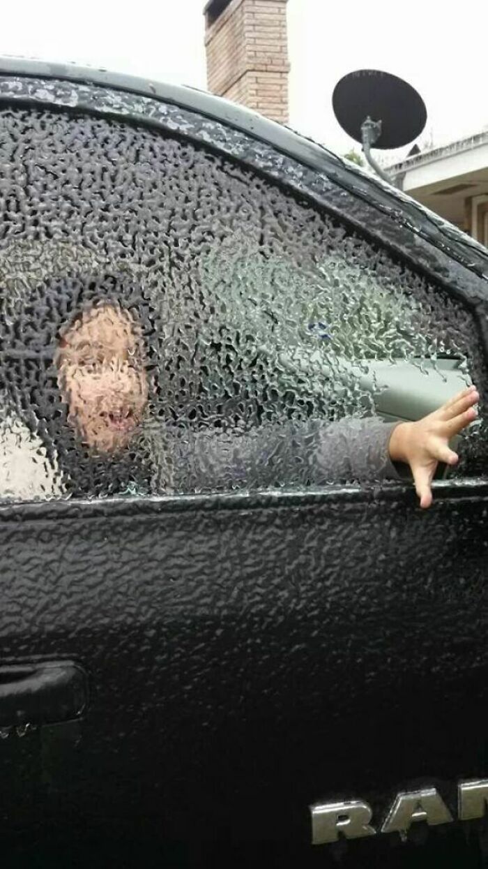 Person inside a car behind an ice-covered window, illustrating ice-cold winter conditions.