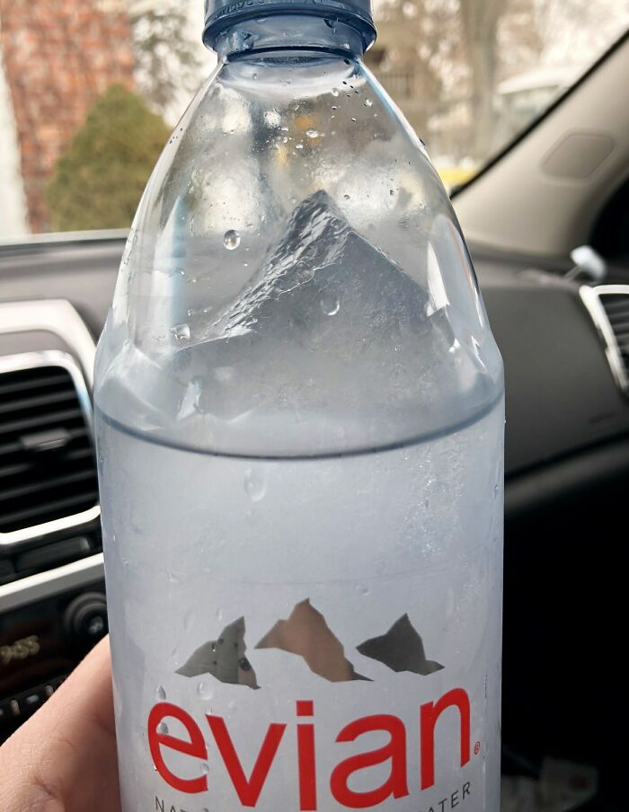 Ice-cold water bottle with ice formation inside, captured in a car with a blurred winter background.