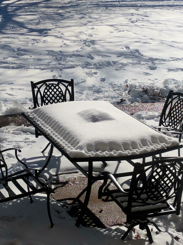 Snow-covered patio table and chairs during a cold winter day, creating a serene outdoor scene.