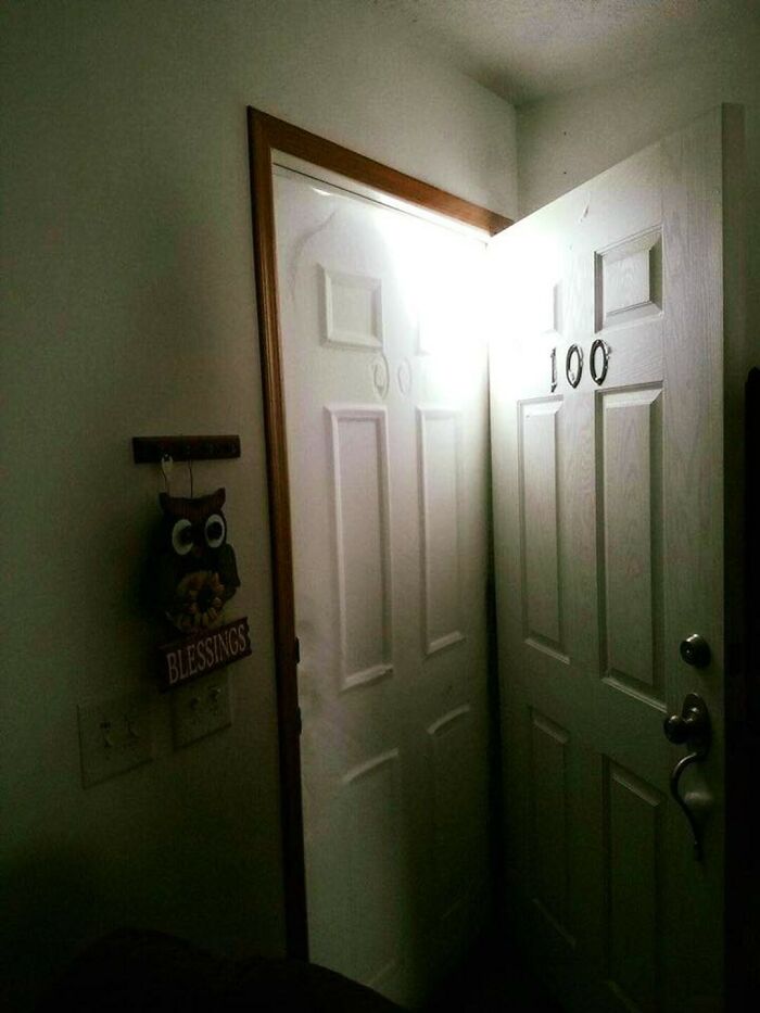 Two white doors with numbers "100" slightly ajar, with a dim indoor setting. Wall decor with an owl and "Blessings" sign.