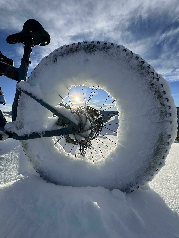 Bicycle wheel covered in snow, capturing the essence of ice-cold winter scenes against a clear sky.