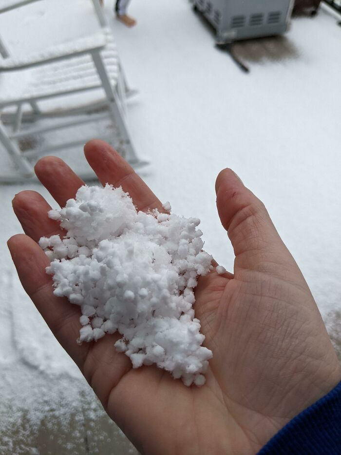 Hand holding ice-cold snow, with wintery backdrop.