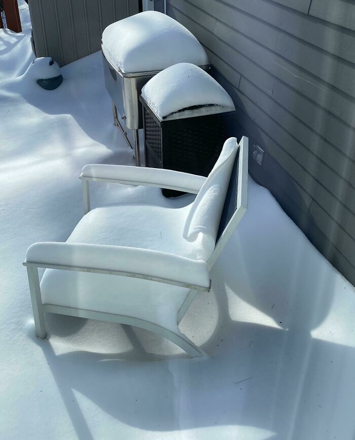 Snow-covered patio chair and outdoor equipment in winter scene.