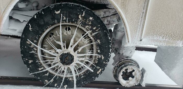 Snow-covered vehicle wheel with icy patterns, showcasing harsh winter conditions.