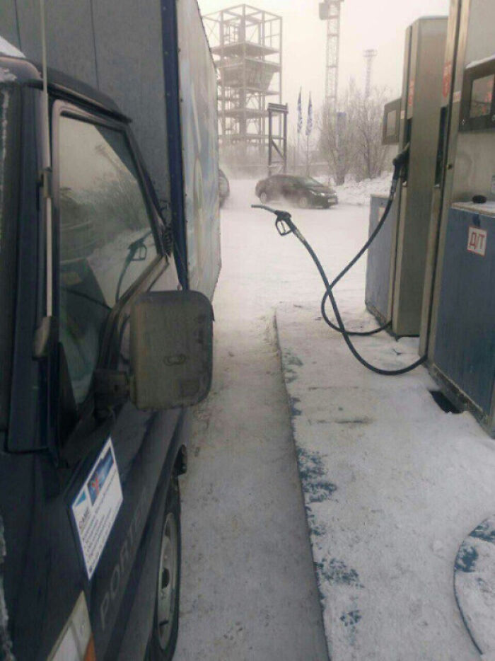 Winter scene at a snowy gas station with a car parked, showcasing ice-cold winter conditions.