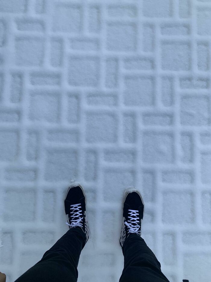 Person wearing black sneakers standing on a snow-covered patterned surface, showcasing ice-cold winter scenery.