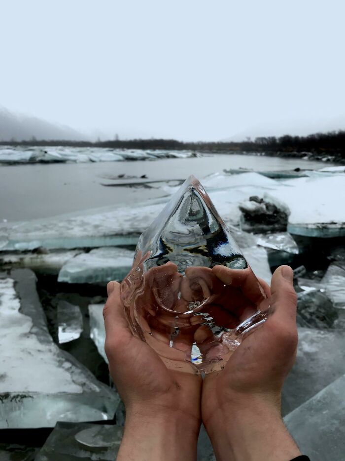 Hands holding an ice shard with a frozen lake in the background, capturing an ice-cold winter scene.