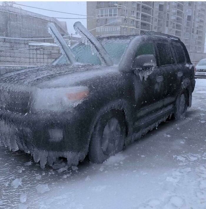 A car covered in ice and snow parked in an urban area, showcasing ice-cold winter conditions.