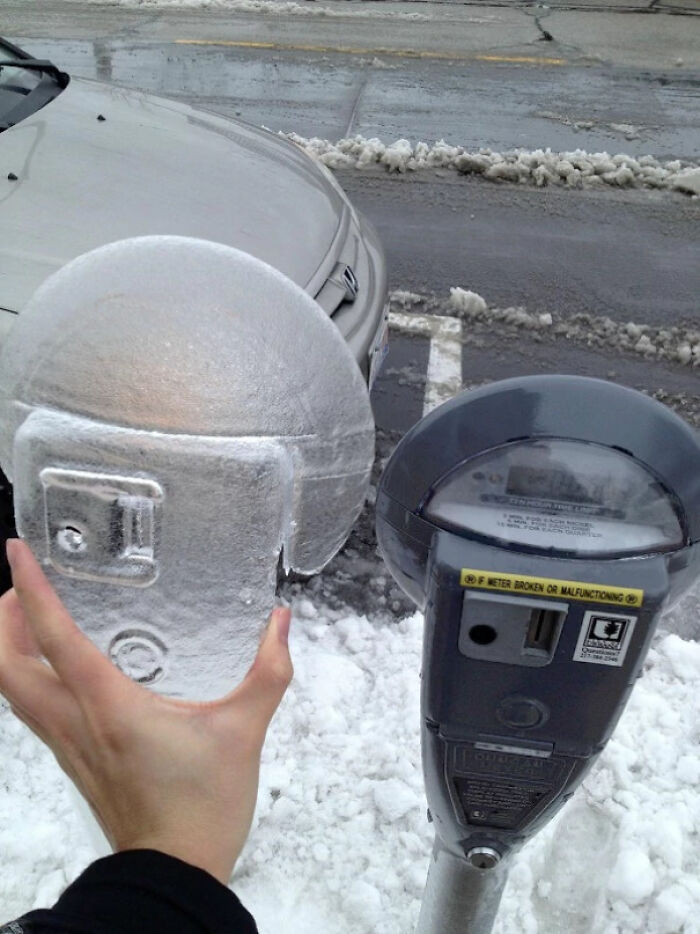 Frozen parking meter lifted in an ice-cold winter setting, snow covering the ground and surrounding areas.