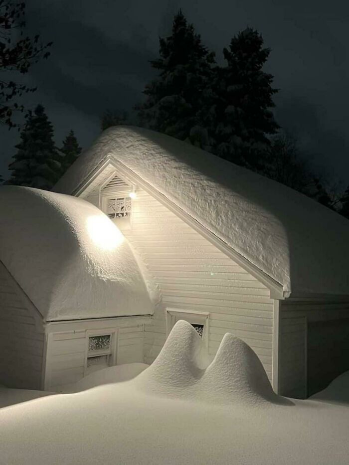 Snow-covered house at night, showcasing ice-cold winter scene with deep drifts under a clear sky.