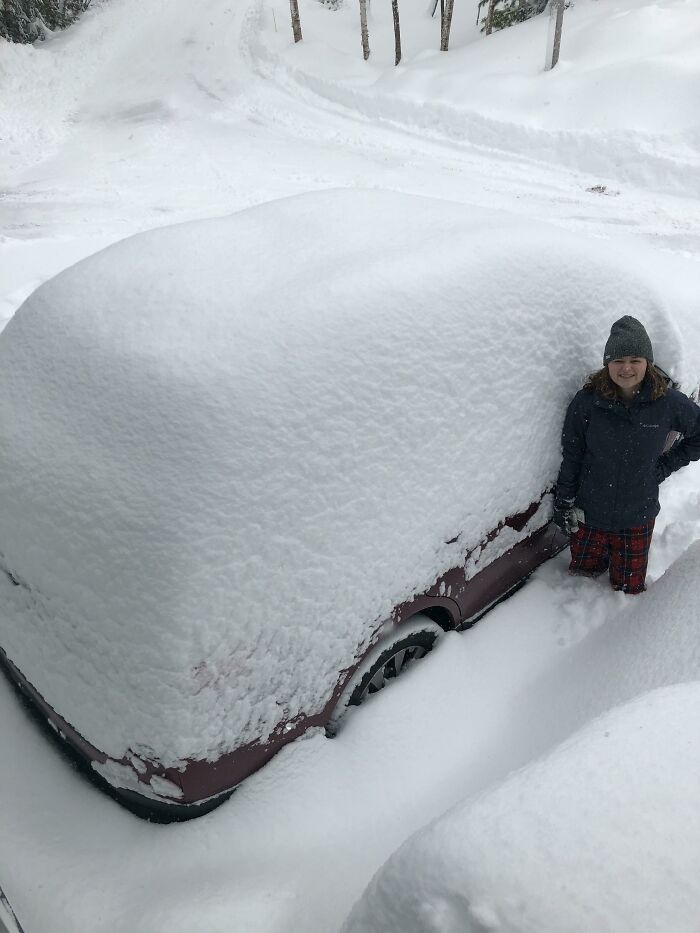 Person in winter clothing standing next to a snow-covered car, showcasing ice-cold winter conditions.