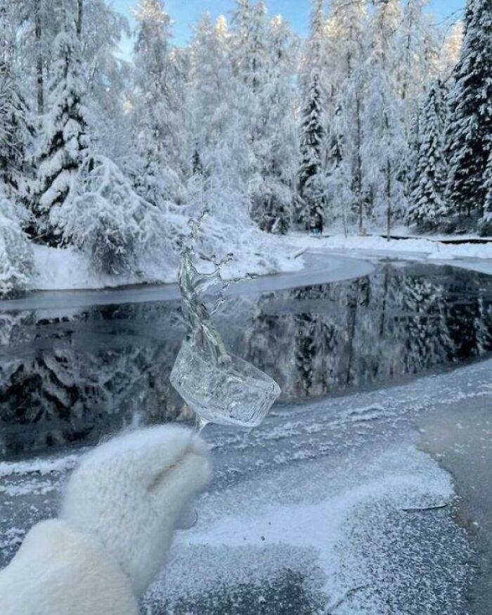 Gloved hand holding ice against a snowy, frozen landscape with trees, embodying ice-cold winter scenes.