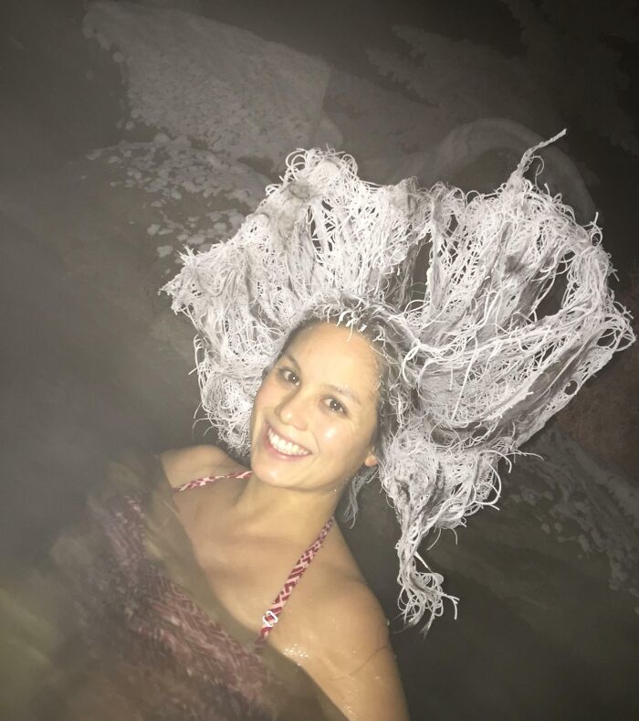 Smiling woman in icy water with frost-covered hair, showcasing an ice-cold winter scene.