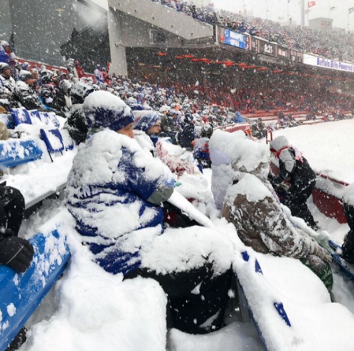 Stadium seats filled with snow-covered spectators during a winter game, highlighting ice-cold winter conditions.