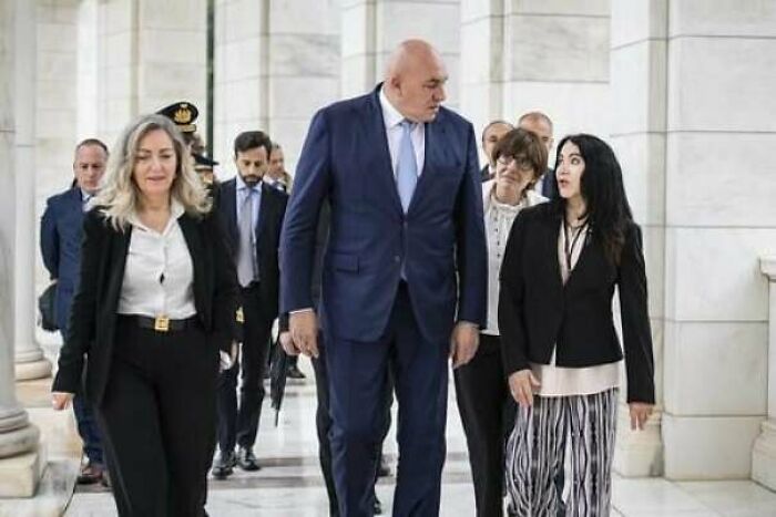 A tall man in a blue suit walking with a group, highlighting absolute units things in a formal setting.