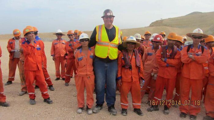 Group of workers in orange uniforms with a tall man in a construction vest, illustrating funny in-law dynamics.