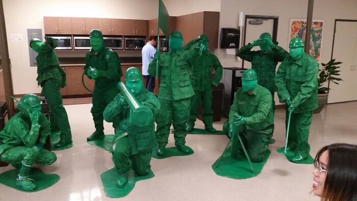 People dressed as green toy soldiers in a humorous group pose at an indoor gathering.