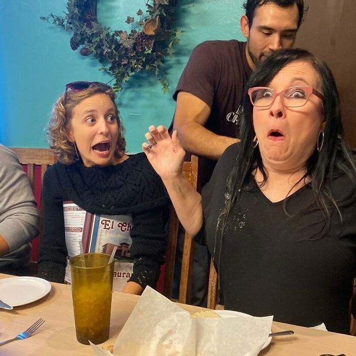 Two women at a table react with surprise, creating a hilarious moment with in-laws.