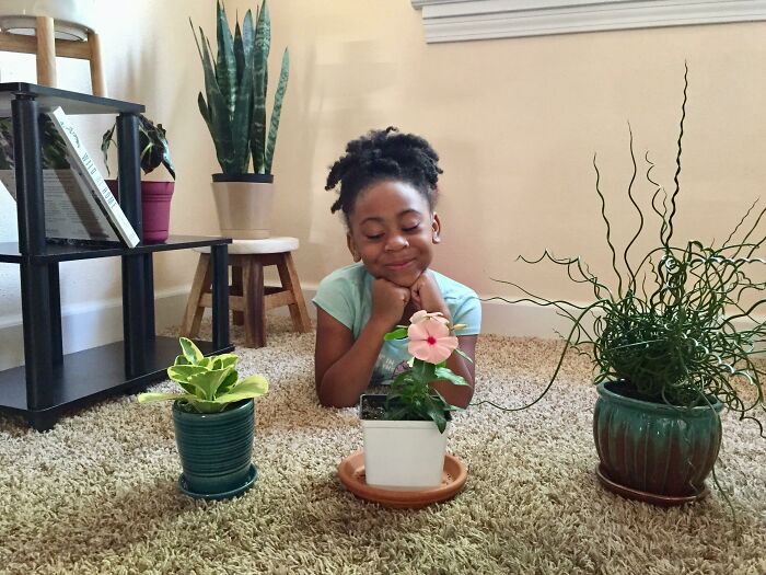 Child smiling with indoor garden plants on carpet in a cozy room.