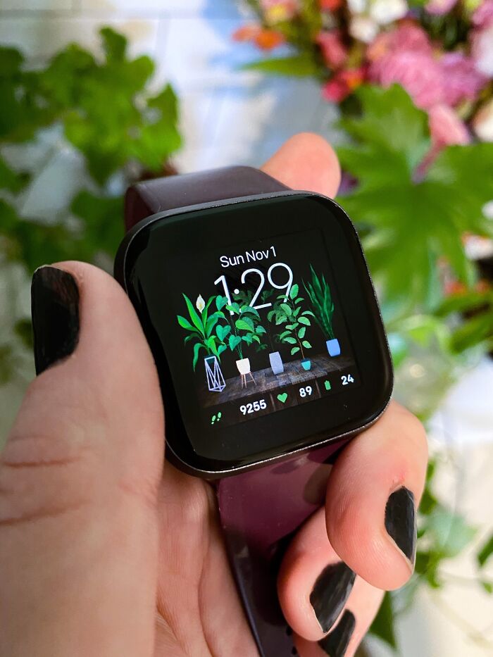 Smartwatch displaying indoor garden plants on screen, held by a person with black nail polish.