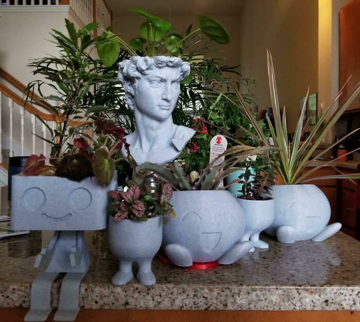 Indoor garden plants in playful pots with a sculpture in the background.