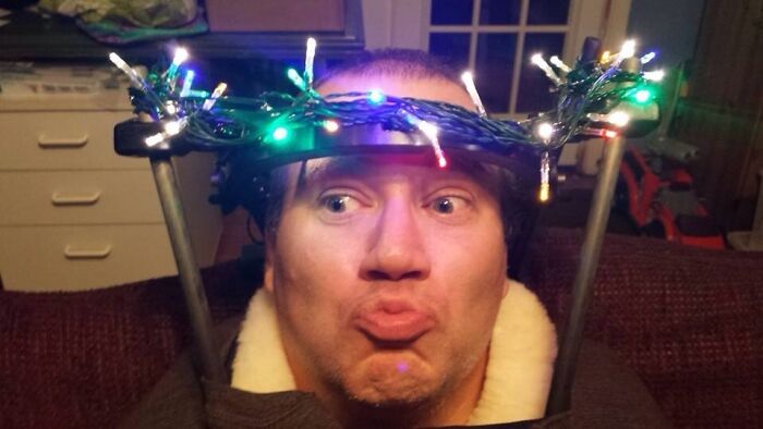 Man making a funny face with holiday lights wrapped around his head, embodying hilarious in-laws humor.