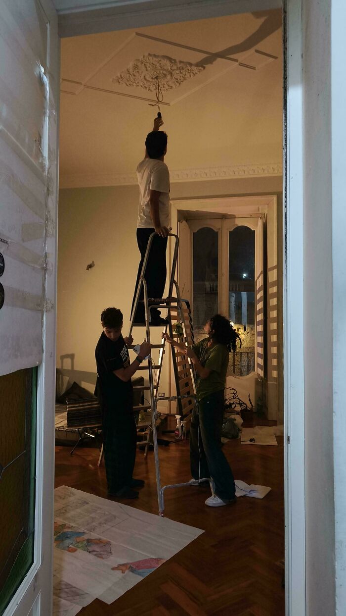 Three people in a room, one on a ladder, unintentionally resembling a Renaissance painting scene.