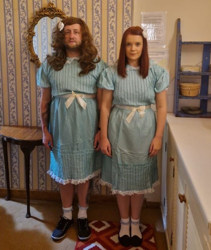 Two people in matching blue dresses pose humorously in a vintage-style room, capturing a hilarious in-laws moment.