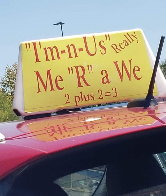 Car rooftop sign with humorous text error: "I'm-n-Us, Me 'R' a We, 2 plus 2 = 3," showcasing a funny ad fail.