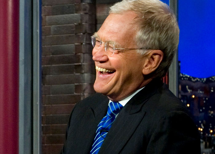 Man in a suit and striped tie laughing during a TV show, representing intriguing facts from the "Today I Learned" community.