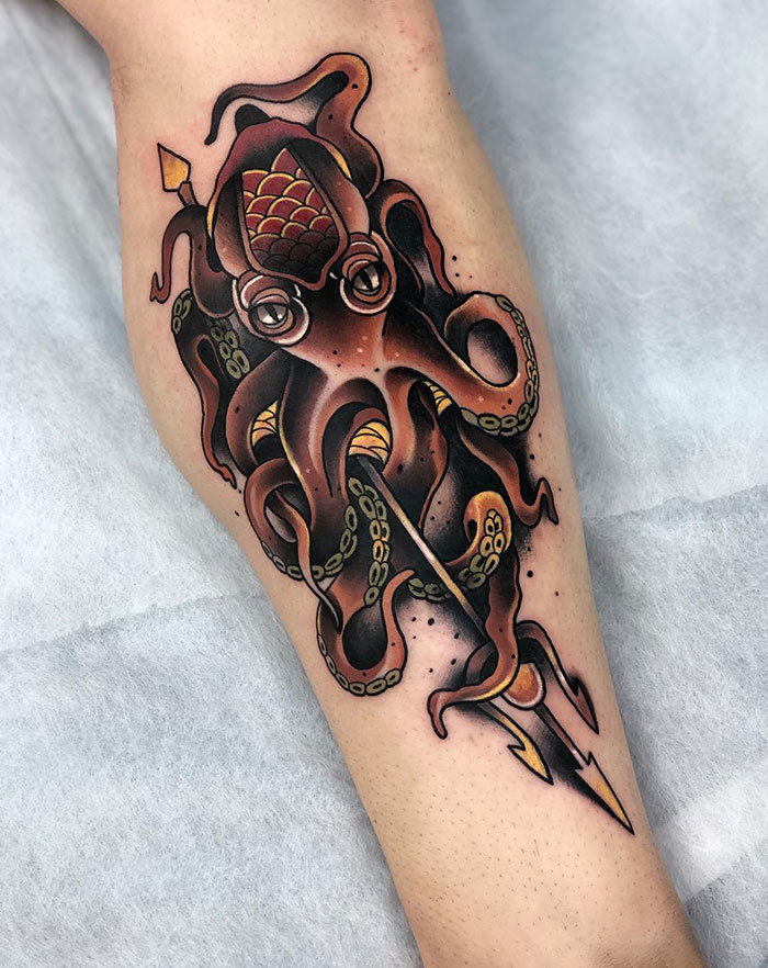 A tattoo of an octopus in traditional American style with detailed shading, wrapped around a trident on a person's leg, featuring bold colors and lines.