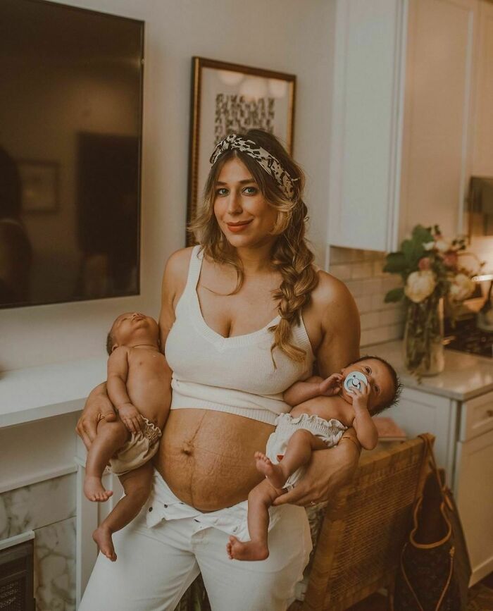 A woman holding two infants in a home setting, showcasing real-life parenting moments.