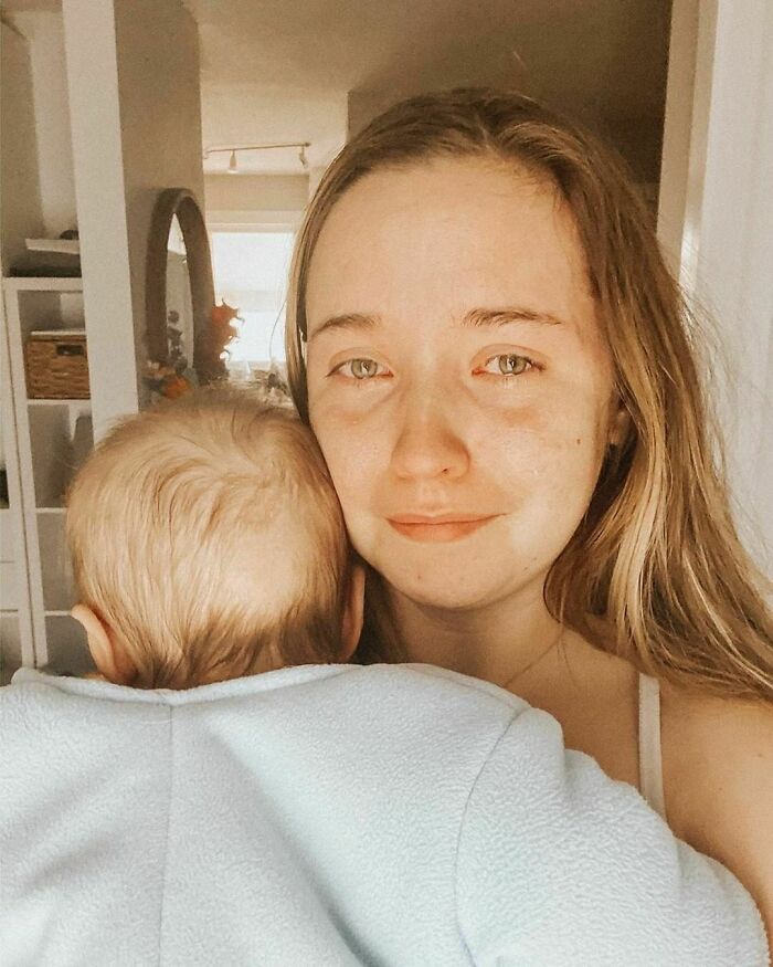 Woman holding a baby, standing in a softly lit room, showcasing a genuine moment of motherhood.