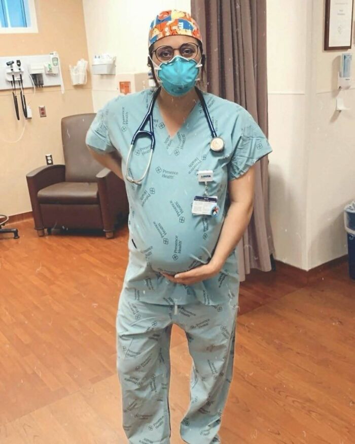 Pregnant healthcare worker in scrubs and mask standing in a hospital room.