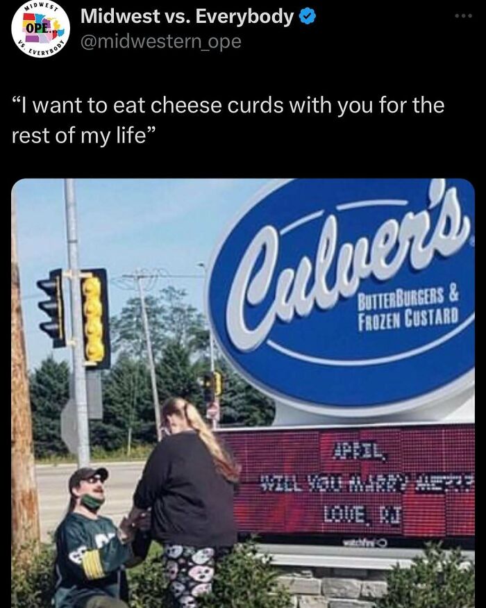 Midwest couple engaged at Culver's sign, reading "April, will you marry me?" with traffic lights and trees in the background.