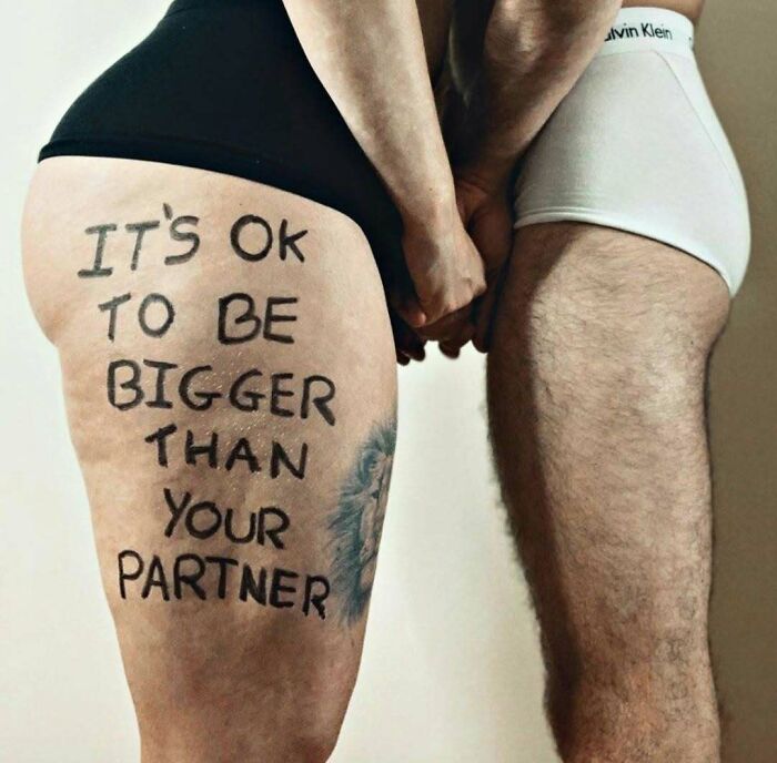 Two people standing close holding hands, with words on a woman's thigh, embodying real-life body positivity.