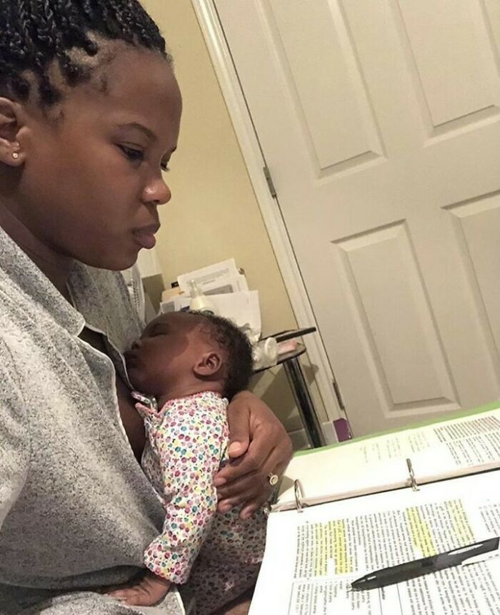 Woman multitasking as she studies with a sleeping baby in her arms, showcasing everyday life balance.