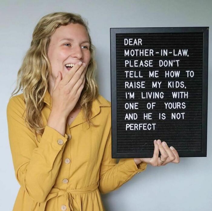 Woman in a yellow dress holding a humorous sign about raising kids, smiling playfully.