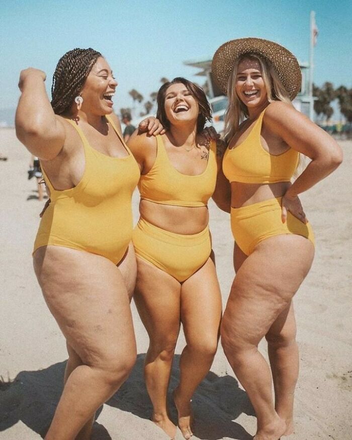 Women in yellow swimsuits laughing together on a sunny beach.