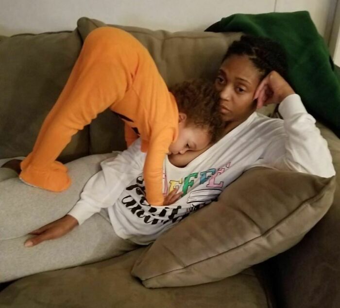 Woman on a couch with a child in orange pajamas lying on her, depicting a real-life moment of parenting.